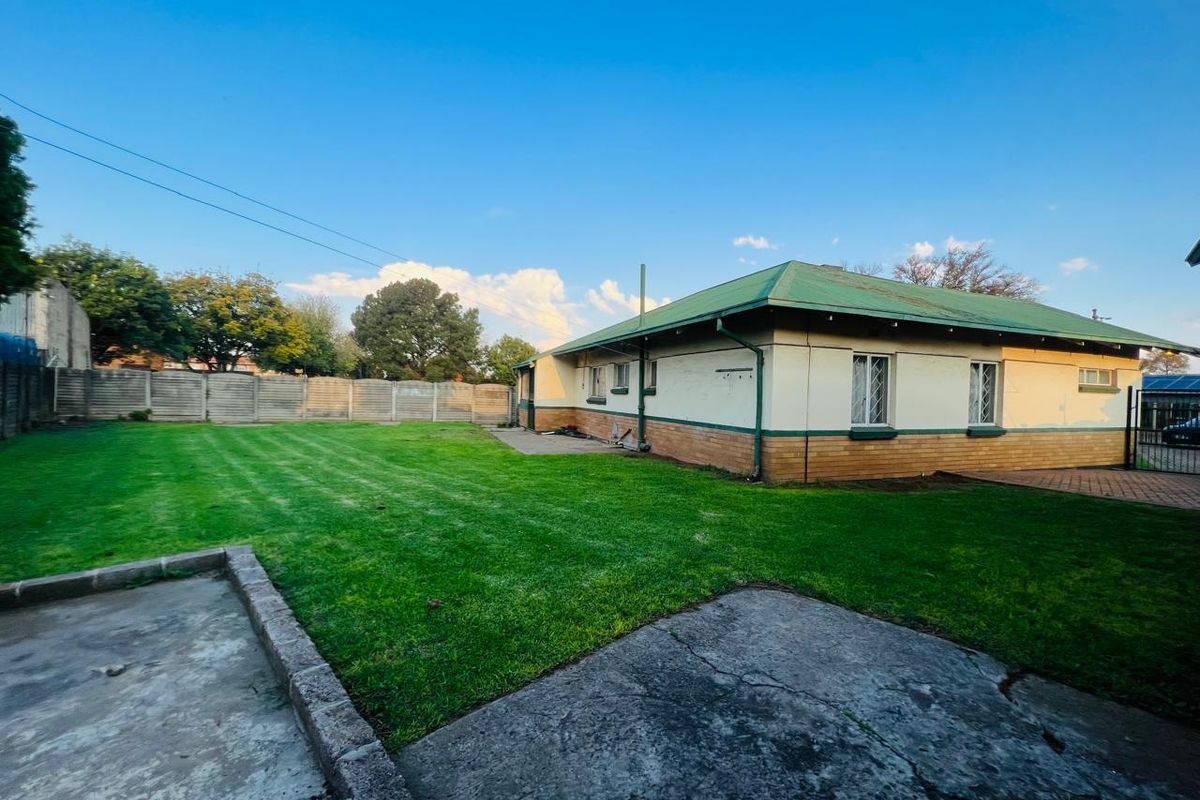 A spacious rear garden featuring a well-maintained lawn, concrete patio area, and a view of the house's rear elevation with a green metal roof.