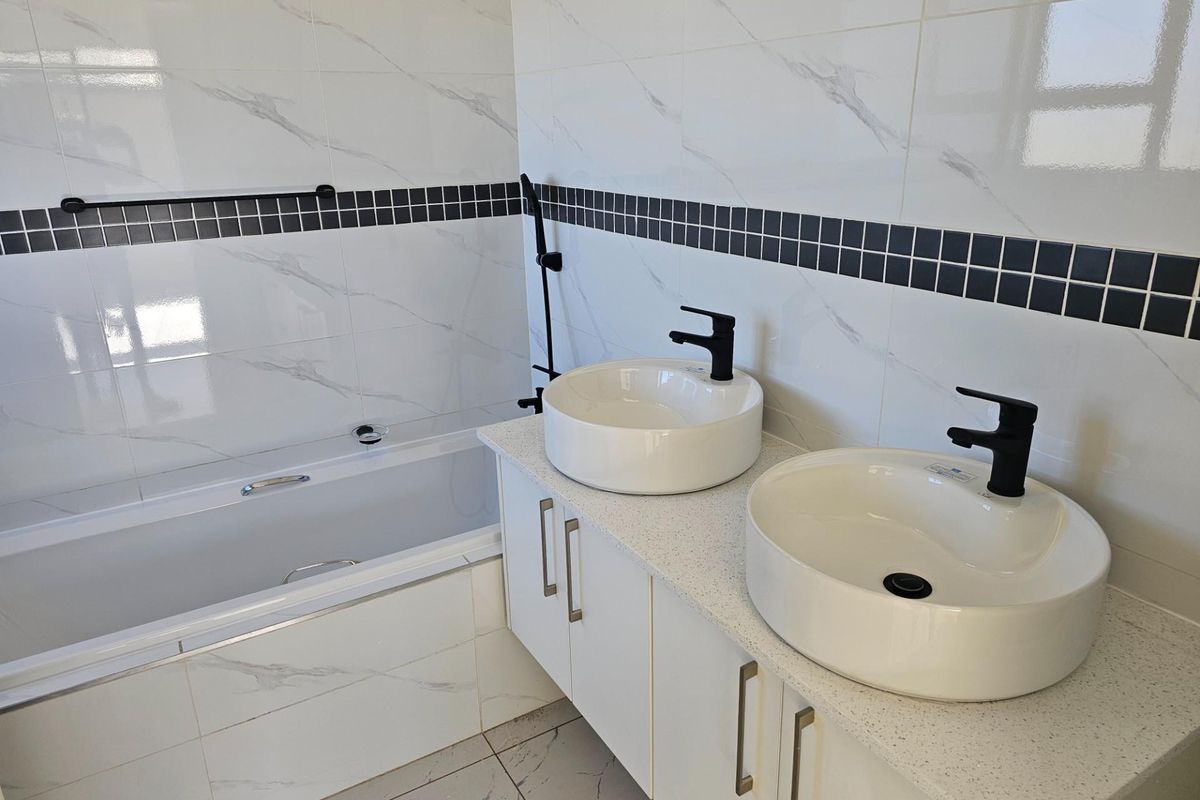 Modern bathroom featuring a double vanity with vessel sinks, matte black fixtures, and a built-in bathtub with marble-look wall tiling.