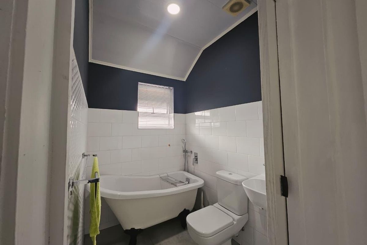 Compact bathroom featuring a classic clawfoot bathtub, white wall tiling, dark accent paint, and modern sanitary fixtures.