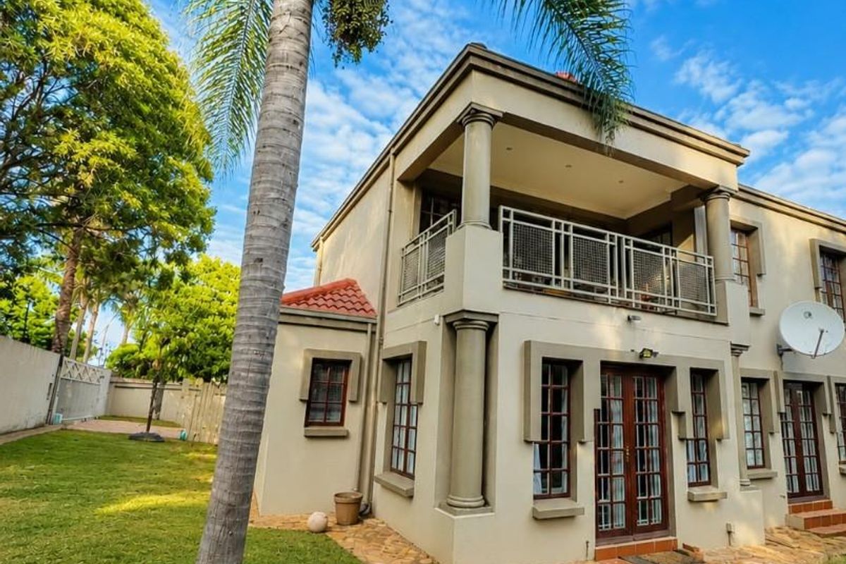 Rear view of a two-story house featuring a balcony with metal railings, stone paved pathways, and a well-maintained garden area.