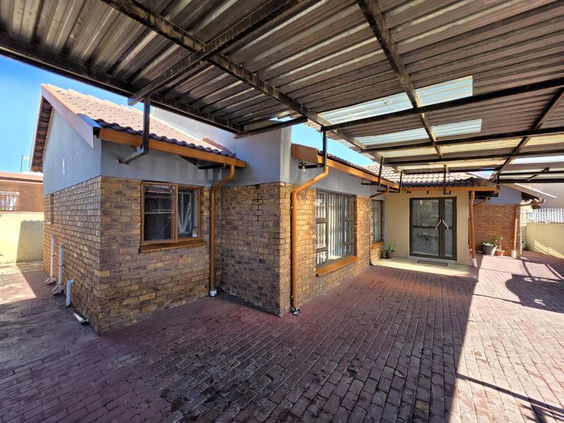 A covered outdoor patio area featuring facebrick walls, paved flooring, and a corrugated metal roof structure with integrated guttering.