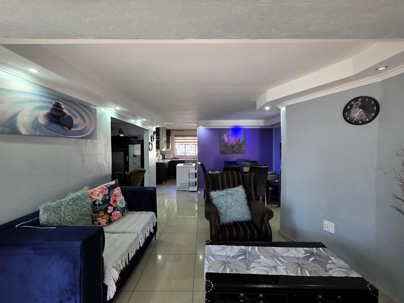An open-plan living and dining area featuring recessed lighting, coved ceilings, and polished floor tiles, flowing into a functional kitchen space.