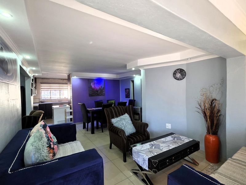 An open-plan living and dining area featuring tiled flooring, recessed ceiling lighting, and a view into the adjacent kitchen space.
