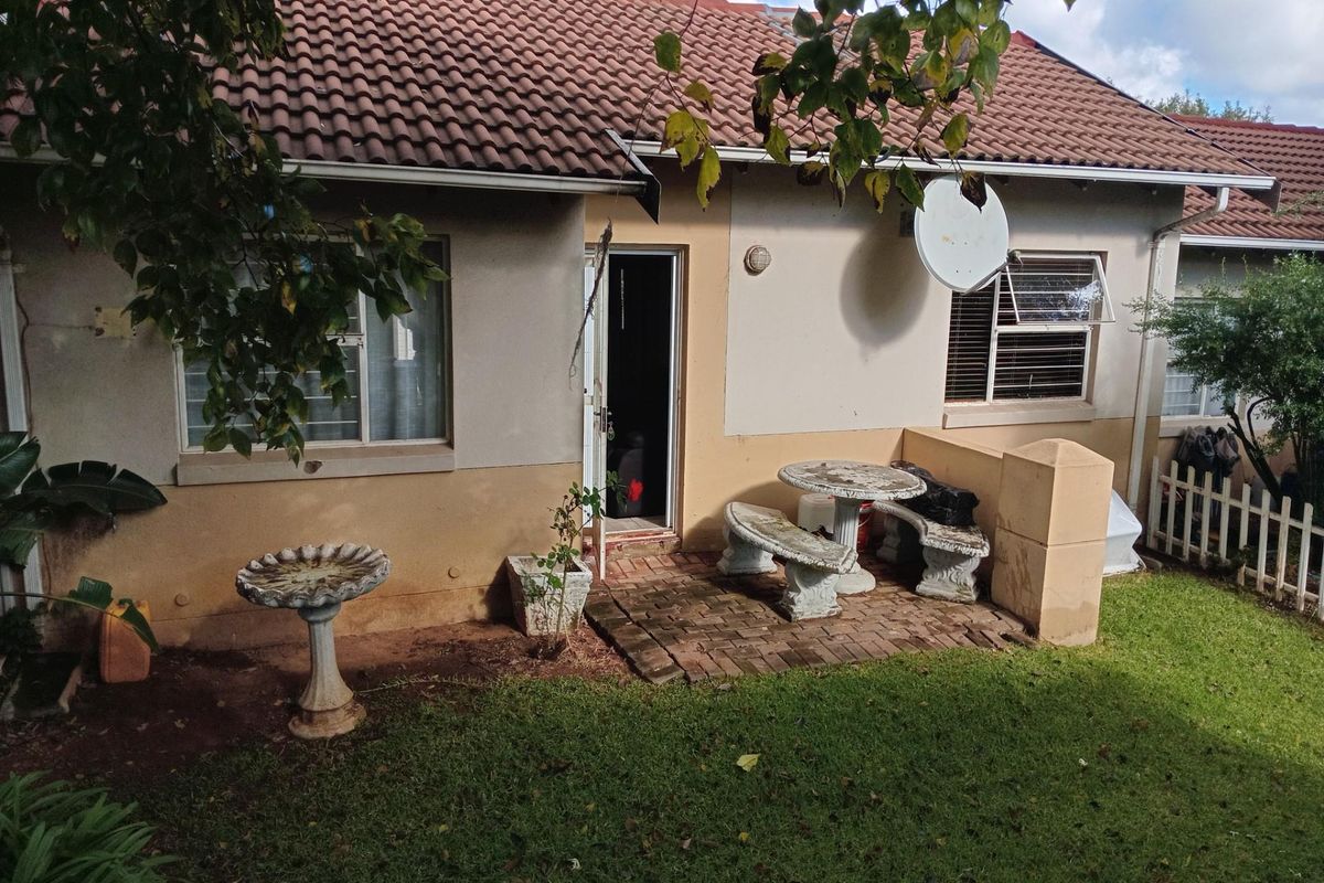 Rear view of the townhouse featuring a paved patio area, tiled roof, and a small private garden space.