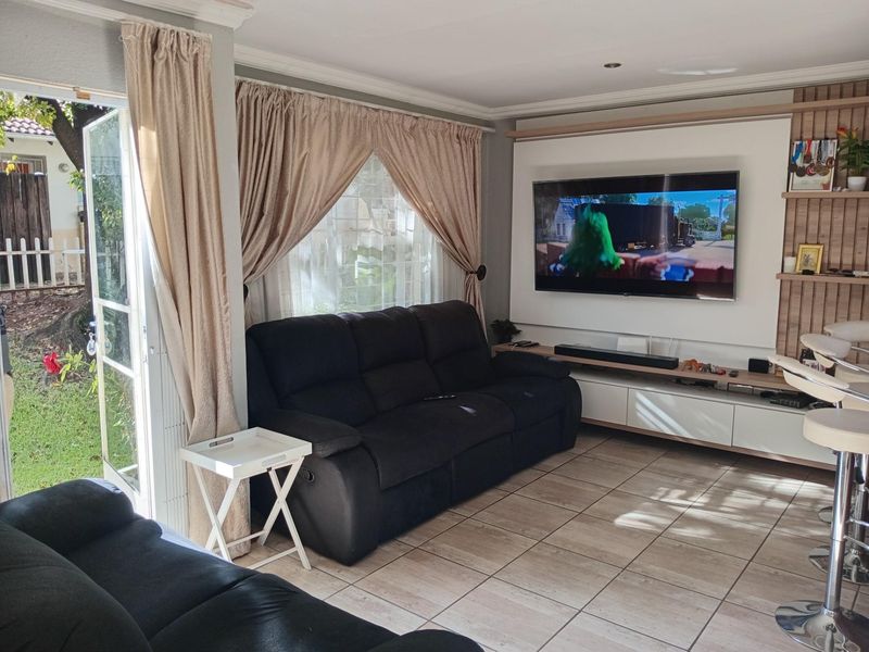 A bright living room featuring tiled flooring, a built-in media wall unit, and direct access to the garden through a glass door.