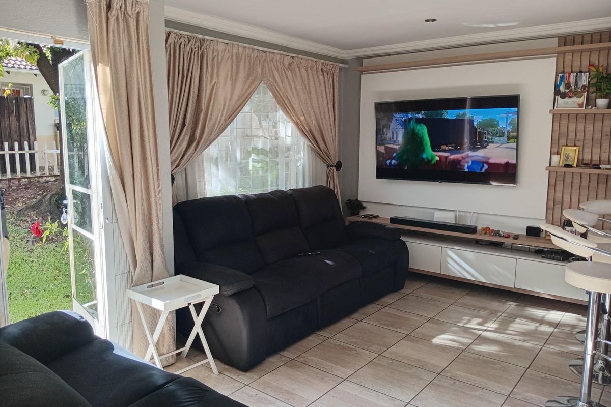A bright living room featuring tiled flooring, a built-in media wall unit, and direct access to the garden through a glass door.