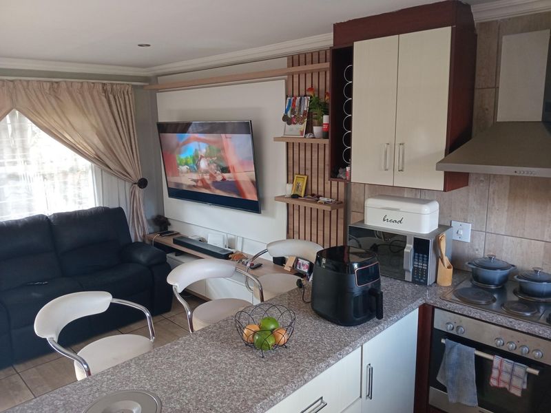 Open-plan living area featuring a compact kitchen with built-in cabinetry, oven, hob, and extractor fan, seamlessly flowing into the adjacent lounge space.