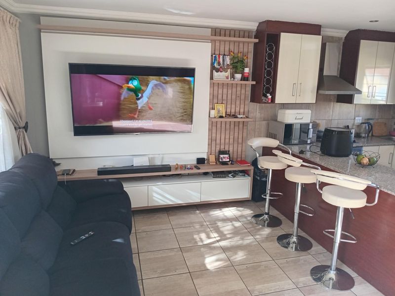 Open-plan living area featuring a modern built-in media unit, tiled flooring, and a kitchen with granite countertops and breakfast bar seating.