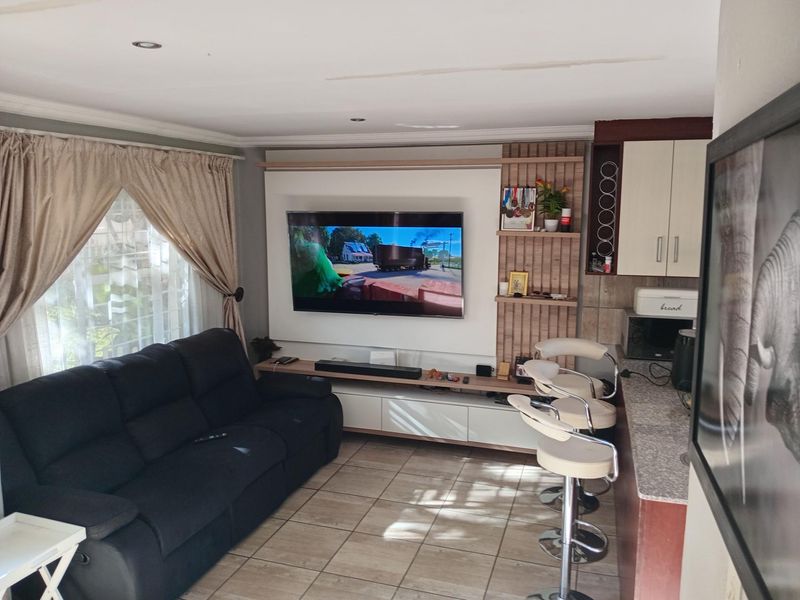 Open-plan living area featuring a built-in media wall unit, tiled flooring, and a breakfast bar counter adjacent to the kitchen space.