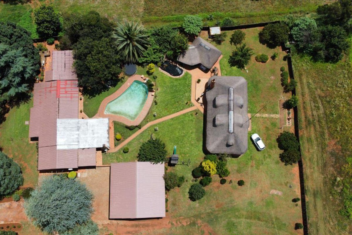 Aerial view of a farm property featuring multiple structures, a swimming pool, and expansive garden grounds.