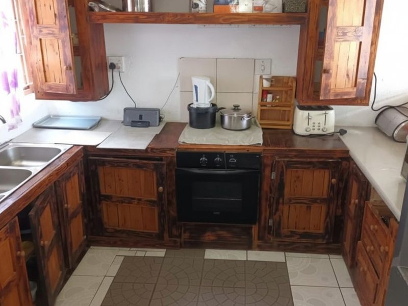 A functional kitchen featuring rustic wooden cabinetry, a built-in oven, and a double-basin stainless steel sink with tiled splashbacks.