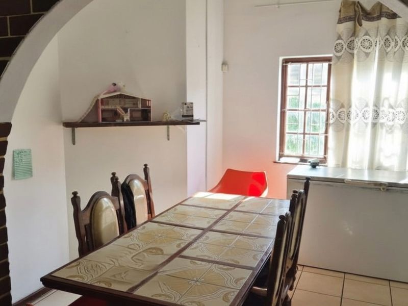 A dining area featuring tiled flooring, a decorative brick-accented archway, and a window providing natural light.