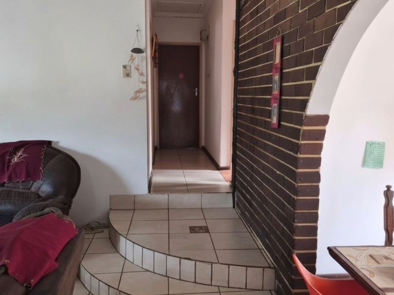 Interior view showing a tiled transition area with a raised step leading into a hallway, featuring a decorative brick archway.