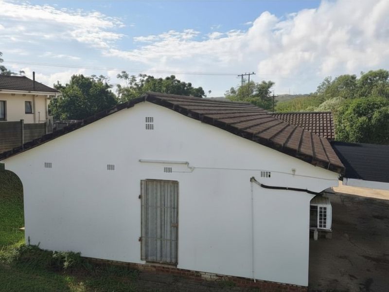 An elevated view of the property's rear exterior, featuring a tiled roof, white rendered walls, and a secure metal door.