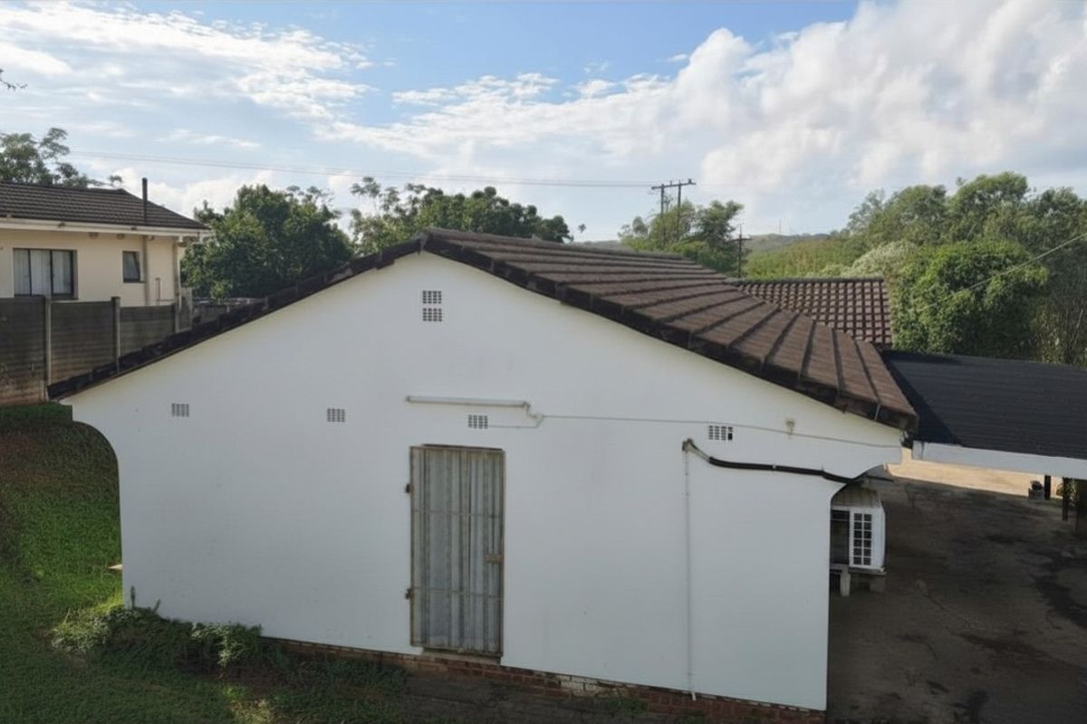 An elevated view of the property's rear exterior, featuring a tiled roof, white rendered walls, and a secure metal door.