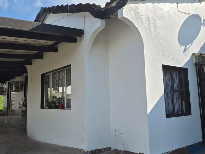 Exterior view of the house featuring a covered carport area, arched architectural detailing, and security bars on the windows.