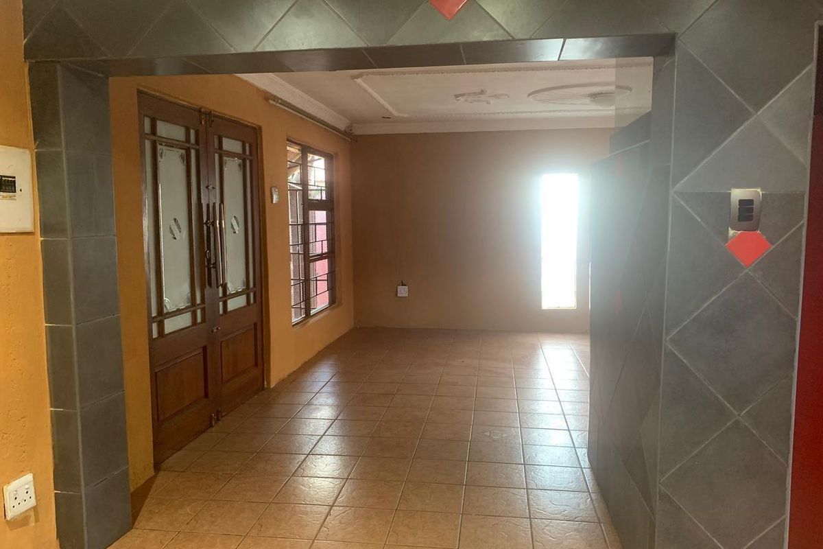An empty living area featuring tiled flooring, decorative ceiling molding, and wooden double doors leading to an adjacent space.