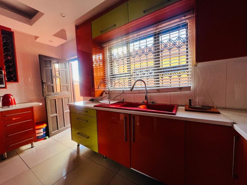 A vibrant kitchen featuring high-gloss red and lime green cabinetry, a double sink, tiled flooring, and a door leading to the exterior.