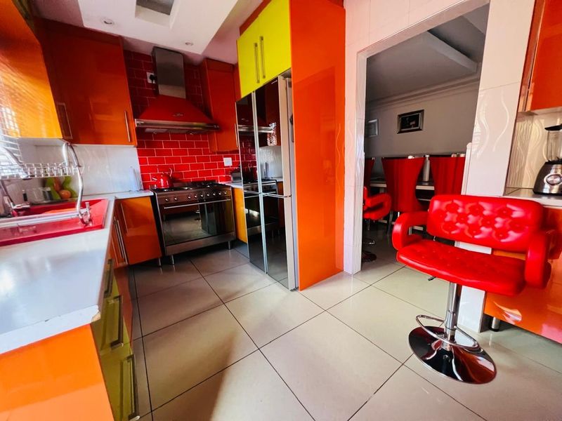 A vibrant kitchen featuring high-gloss orange and yellow cabinetry, a stainless steel gas stove with extractor fan, and tiled flooring.