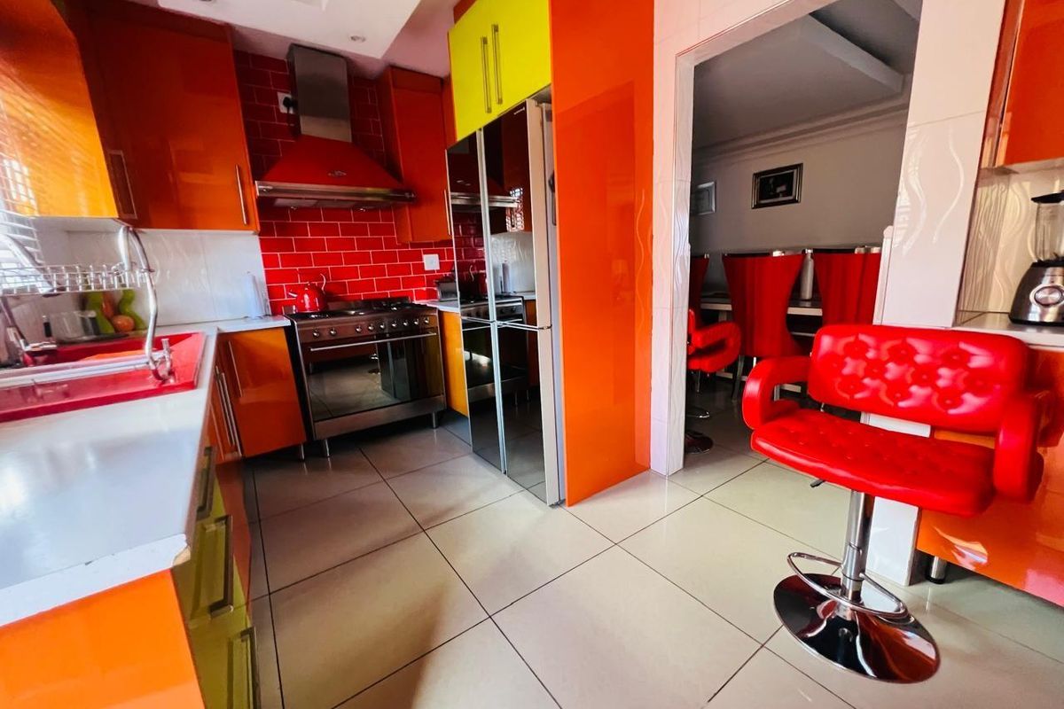 A vibrant kitchen featuring high-gloss orange and yellow cabinetry, a stainless steel gas stove with extractor fan, and tiled flooring.