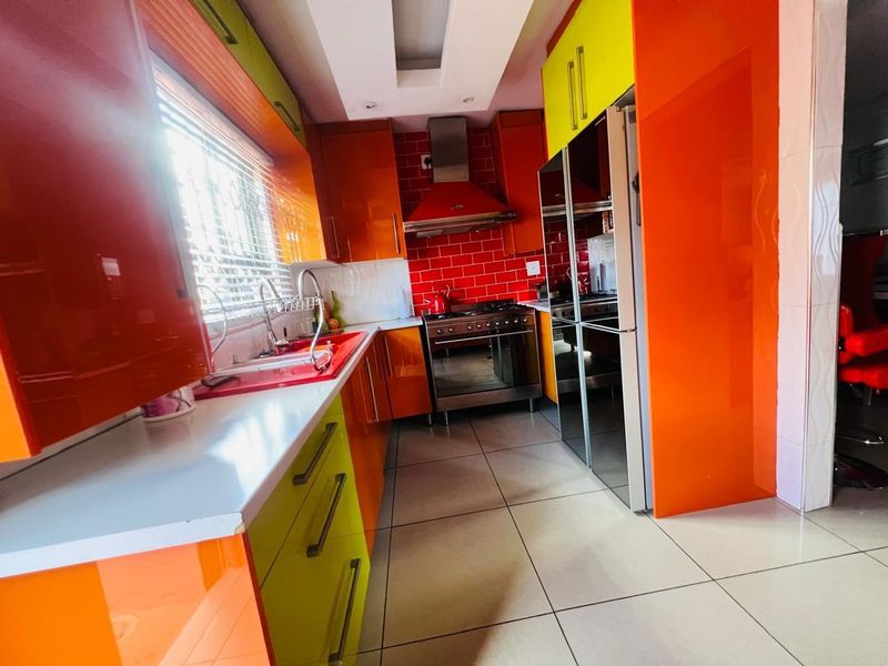 A vibrant kitchen featuring high-gloss orange and lime green cabinetry, a stainless steel gas stove with extractor fan, and red subway tile backsplash.