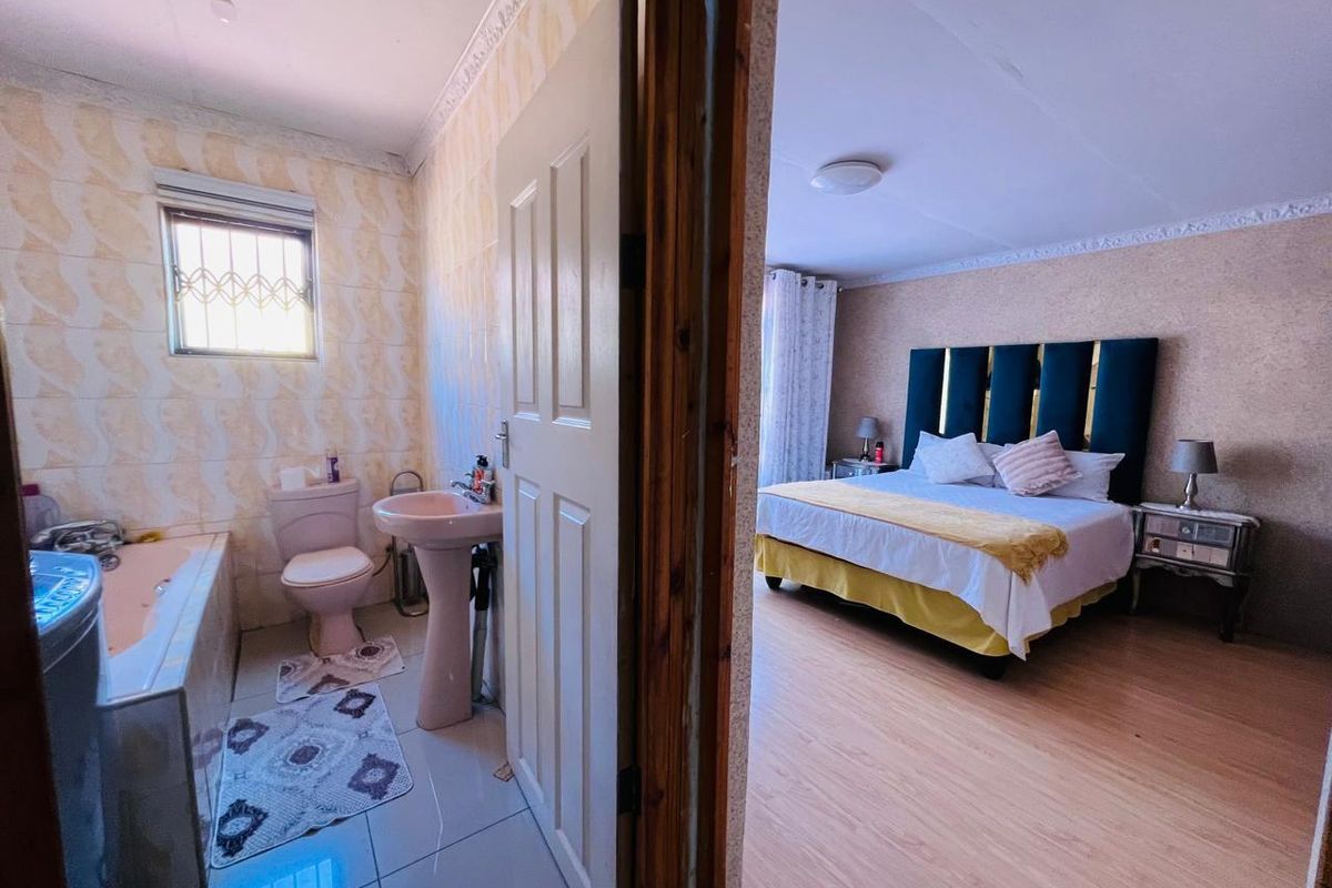 A view from a bedroom into an adjacent bathroom featuring a bathtub, pedestal sink, and toilet with tiled walls.
