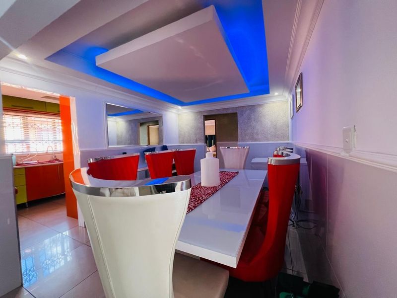 A dining area featuring a modern tray ceiling with integrated blue LED lighting, tiled flooring, and a view into the adjacent kitchen space.