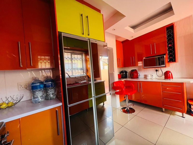 A vibrant kitchen featuring high-gloss orange cabinetry, contrasting lime green accents, tiled flooring, and integrated built-in appliances.