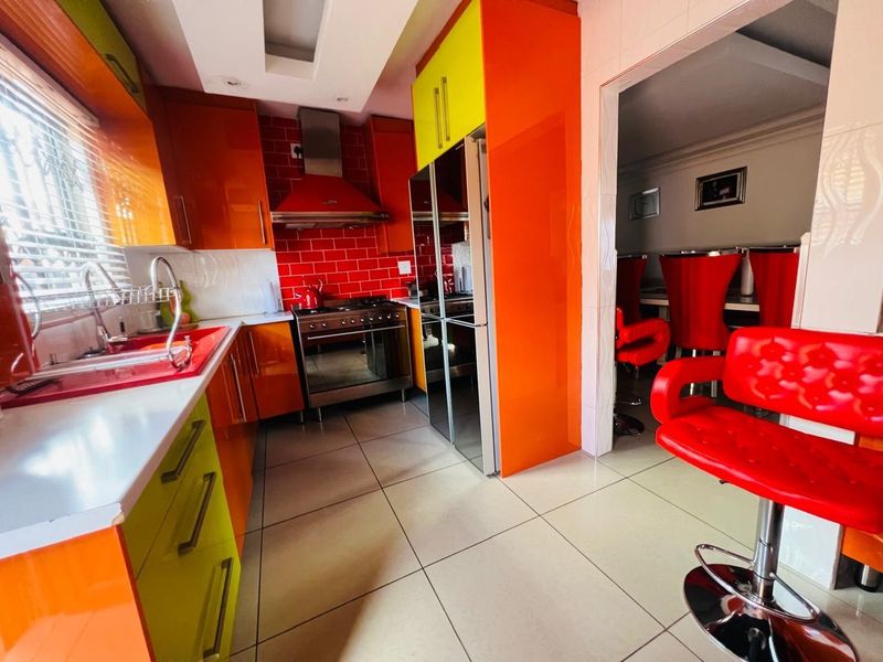 A vibrant kitchen featuring high-gloss orange and lime cabinetry, a red subway tile backsplash, stainless steel extractor fan, and tiled flooring.