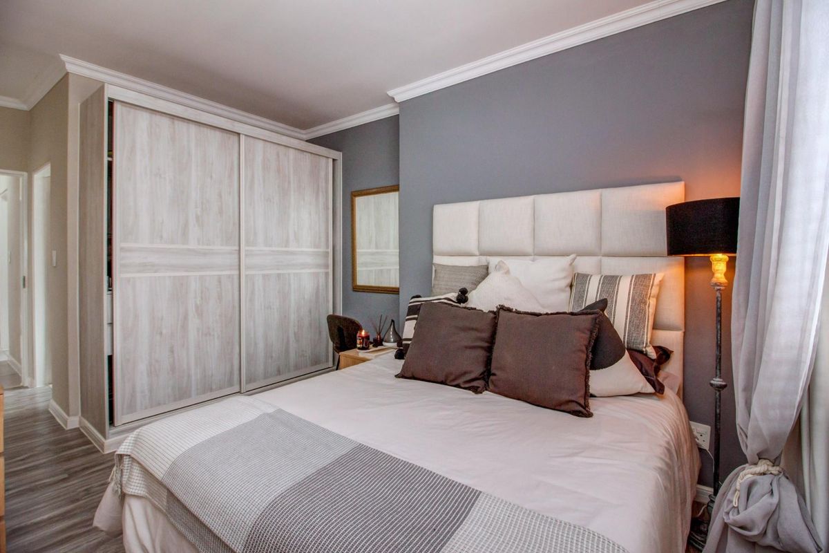 A well-maintained bedroom featuring built-in sliding door wardrobes, crown molding, and neutral grey wall finishes.