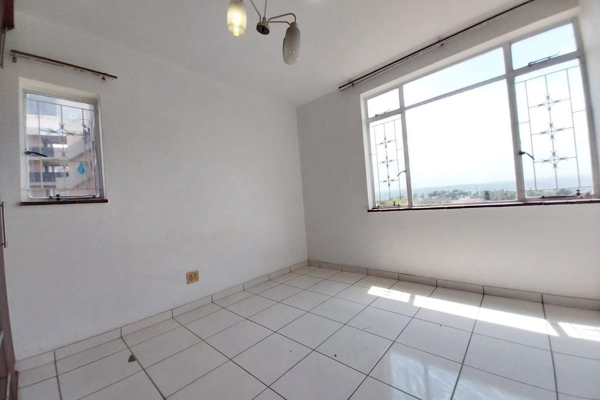 A bright, empty bedroom featuring white tiled flooring, large windows with security bars, and a central ceiling light fixture.