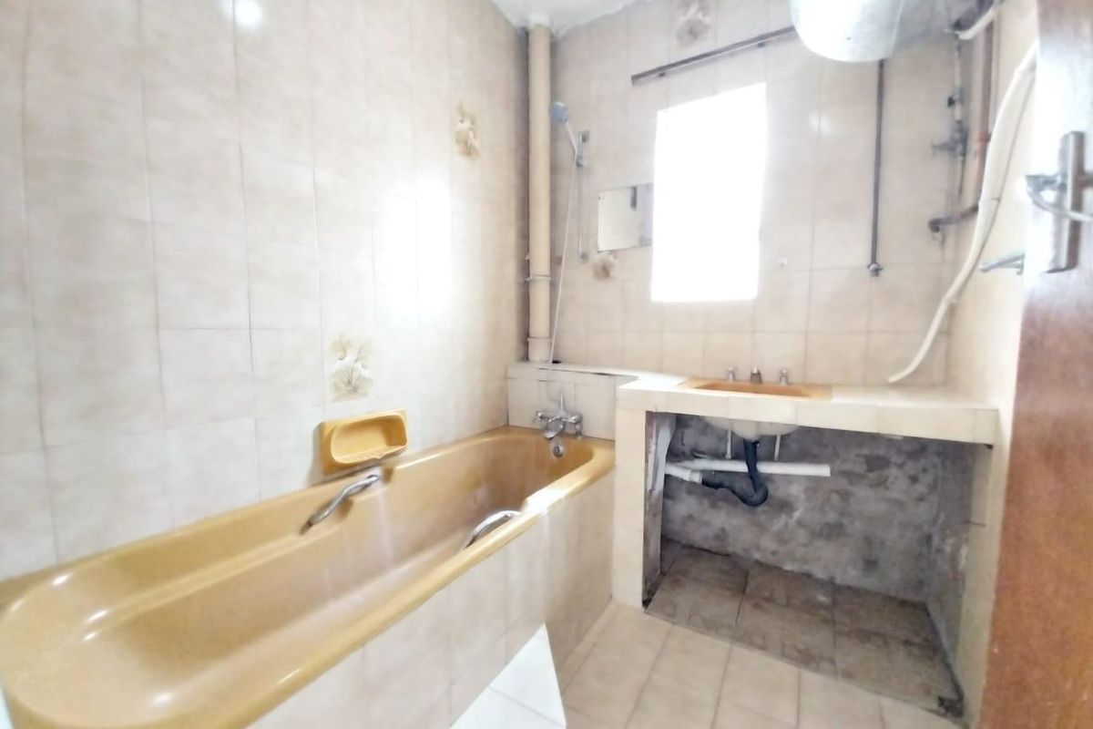 A dated bathroom featuring a built-in bathtub and a vanity area with exposed plumbing and unfinished cabinetry, requiring renovation.