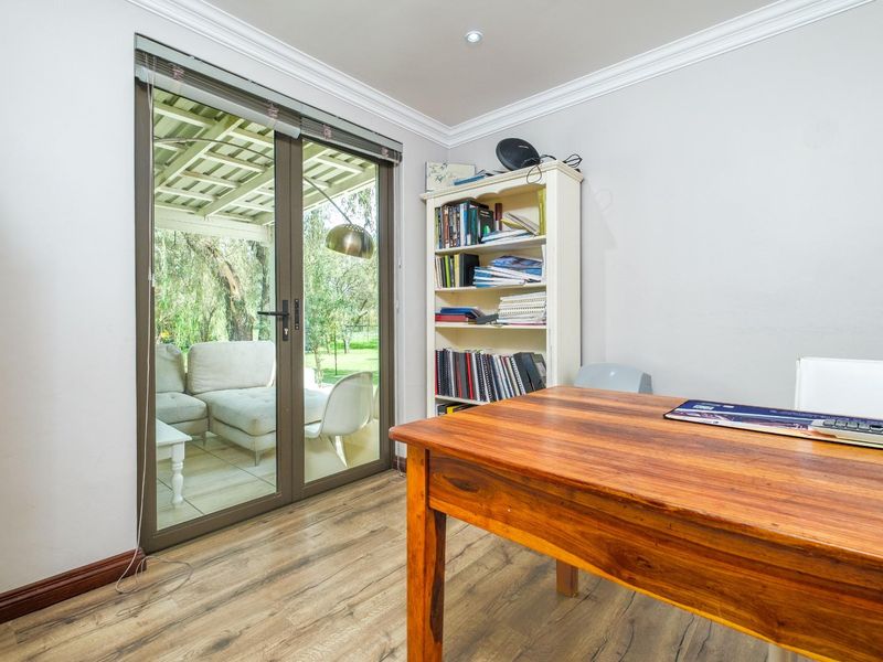 A bright home office featuring wood-look flooring, crown molding, and sliding glass doors that provide direct access to a covered patio.