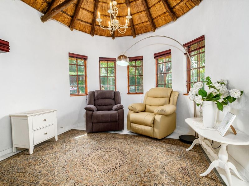 A circular living area featuring a traditional thatched roof, exposed timber beams, and multiple windows providing natural light.