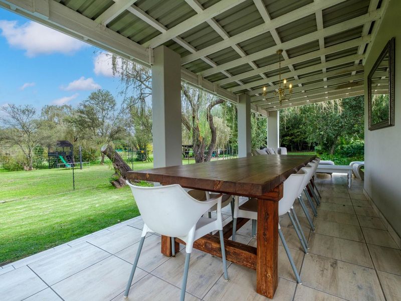 Spacious covered patio featuring tiled flooring and a ceiling-mounted chandelier, overlooking a large, well-maintained garden area.