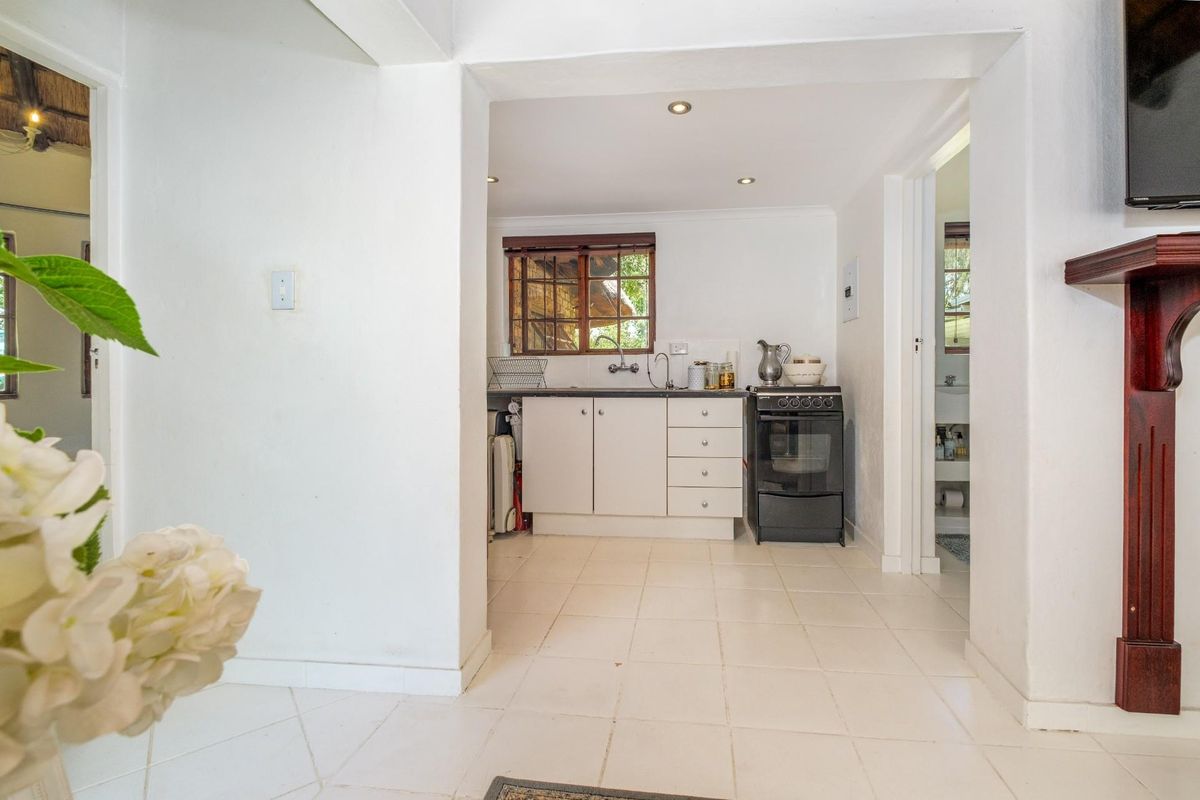 A compact kitchen area featuring white cabinetry, a freestanding stove, and tiled flooring, viewed from an adjacent living space.