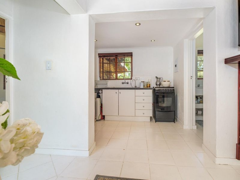 A compact kitchen area featuring white cabinetry, a freestanding stove, and tiled flooring, viewed from an adjacent living space.