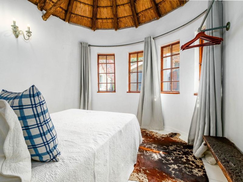 A unique circular bedroom featuring a traditional thatched roof, timber-framed windows, and wall-mounted lighting in a cozy, rustic setting.