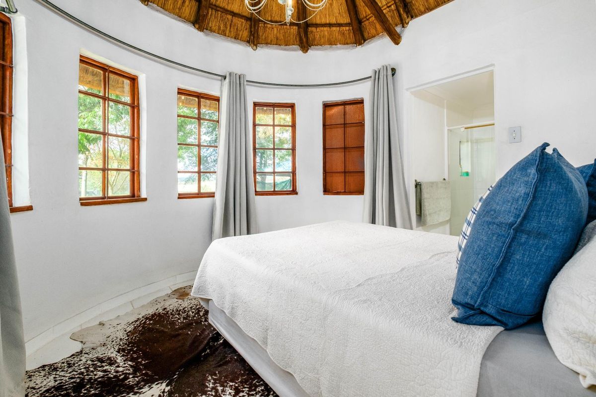A circular bedroom featuring a traditional thatched roof, timber-framed windows, and an en-suite bathroom access.