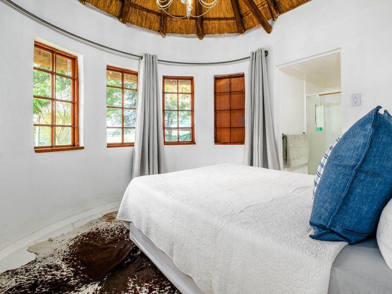 A circular bedroom featuring a traditional thatched roof, timber-framed windows, and an en-suite bathroom access.