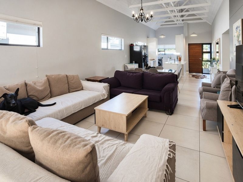 Spacious open-plan living and dining area featuring high vaulted ceilings with exposed trusses, tiled flooring, and a modern integrated kitchen.