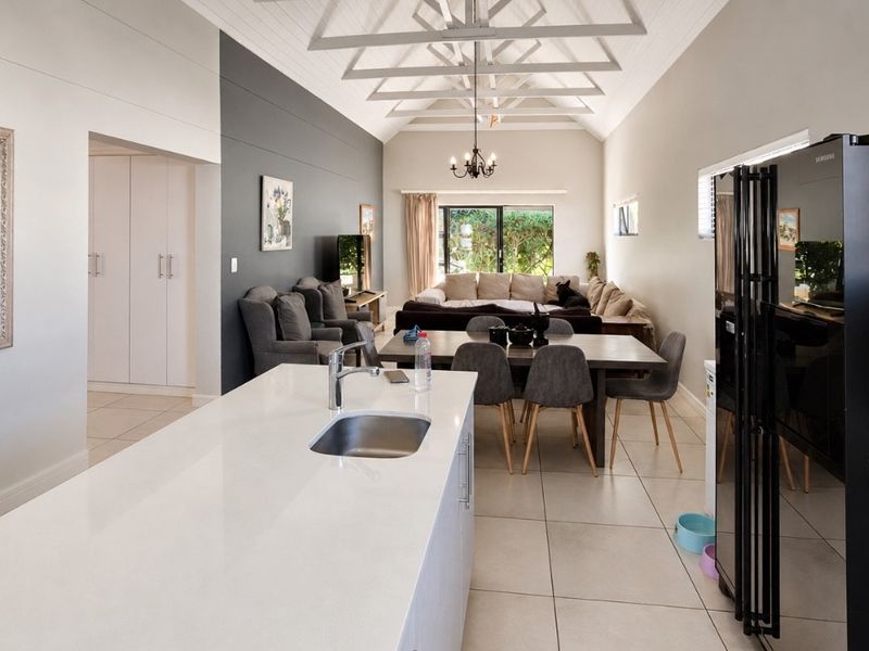 Spacious open-plan living area featuring a modern kitchen island, vaulted ceilings with exposed rafters, and seamless flow to the outdoor patio area.