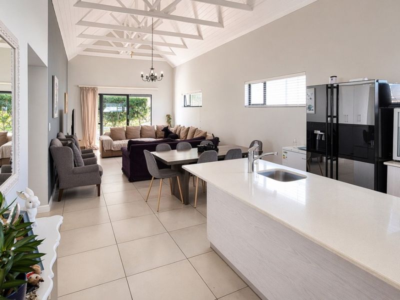 Spacious open-plan living area featuring a modern kitchen island, high vaulted ceilings with exposed trusses, and large sliding doors leading to the garden.