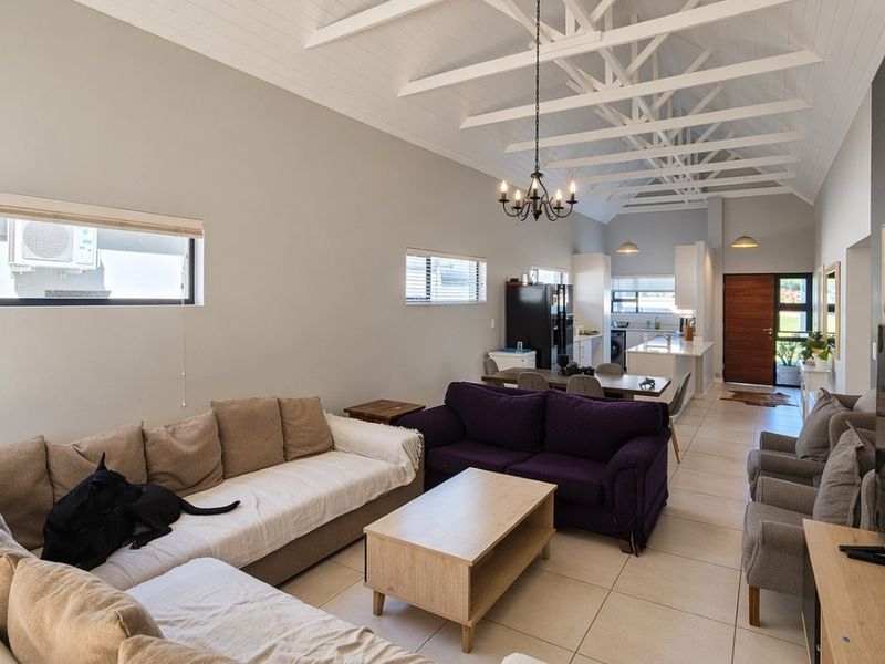 Spacious open-plan living and dining area featuring high vaulted ceilings with exposed trusses, tiled floors, and a modern kitchen with a central island.