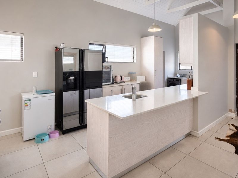 Modern kitchen featuring a central island with stone countertops, light wood cabinetry, vaulted ceilings, and tiled flooring, providing a bright and functional workspace.
