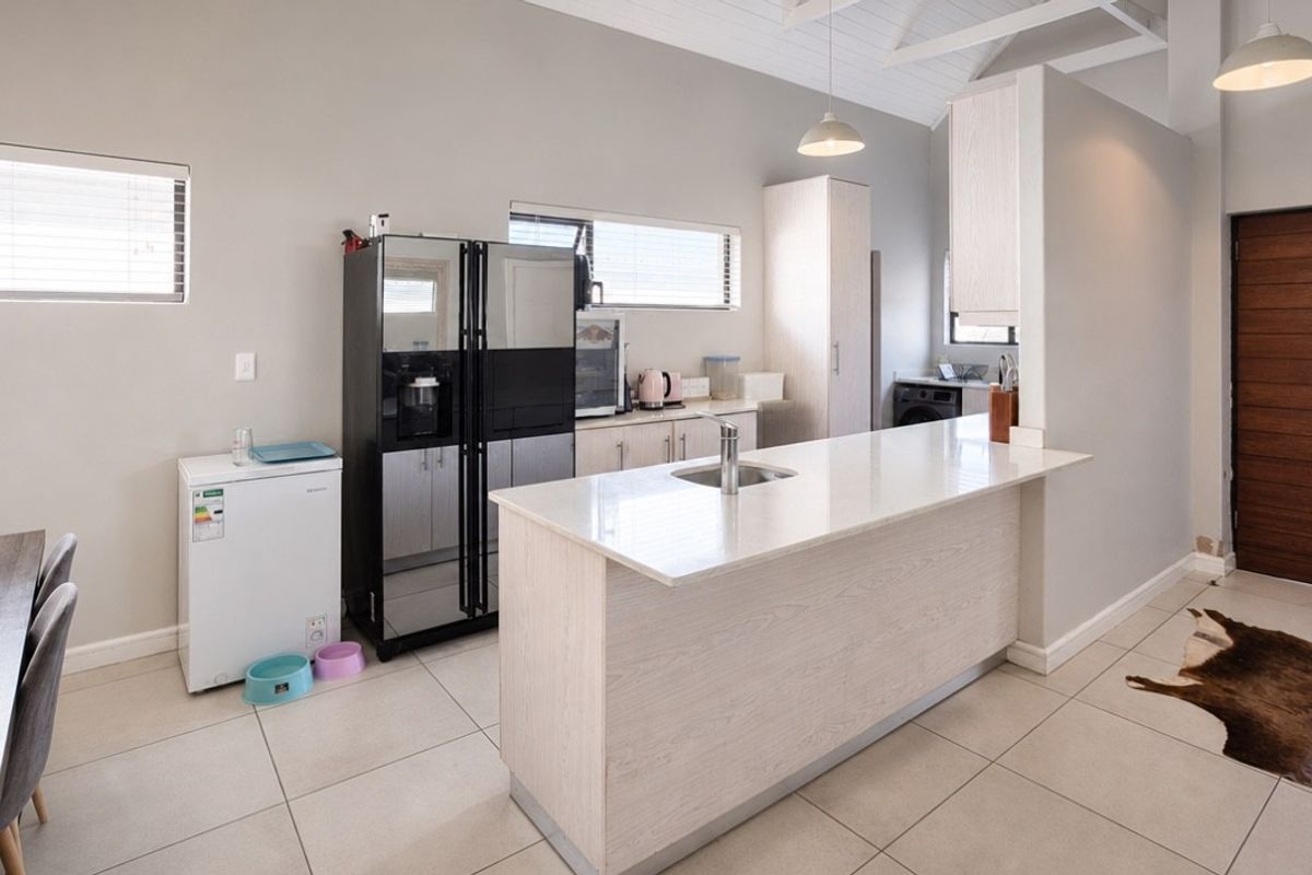 Modern kitchen featuring a central island with stone countertops, light wood cabinetry, vaulted ceilings, and tiled flooring, providing a bright and functional workspace.