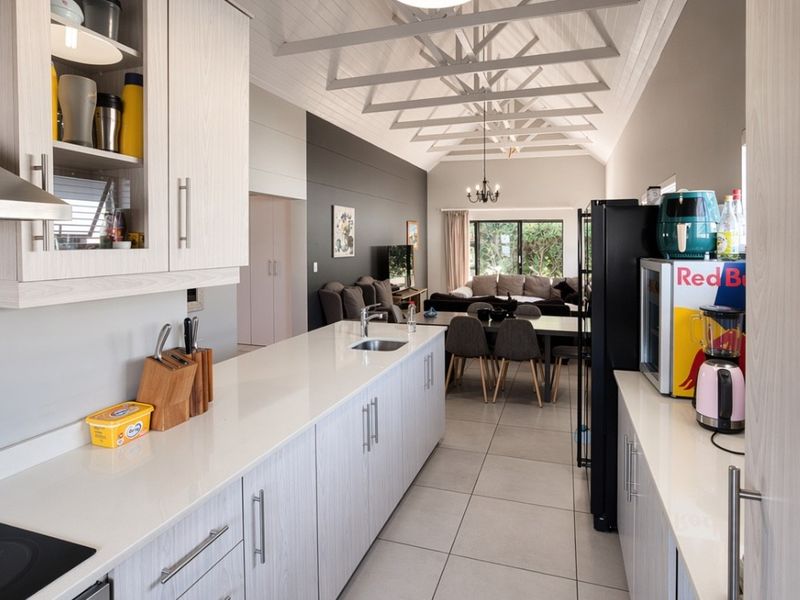 Modern open-plan kitchen and living area featuring light wood cabinetry, quartz countertops, exposed roof trusses, and neutral tiled flooring.