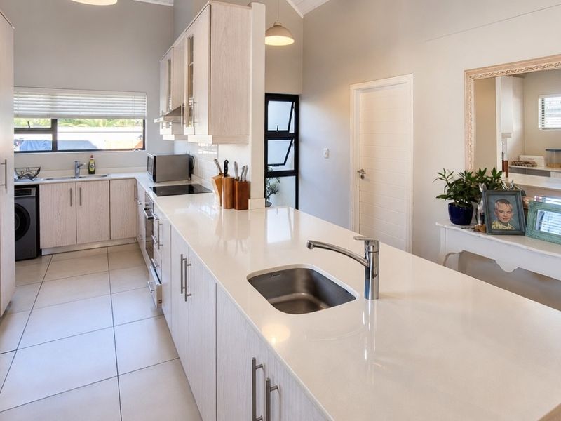 Modern kitchen featuring light wood-grain cabinetry, white quartz countertops, integrated appliances, and tiled flooring with a functional island layout.