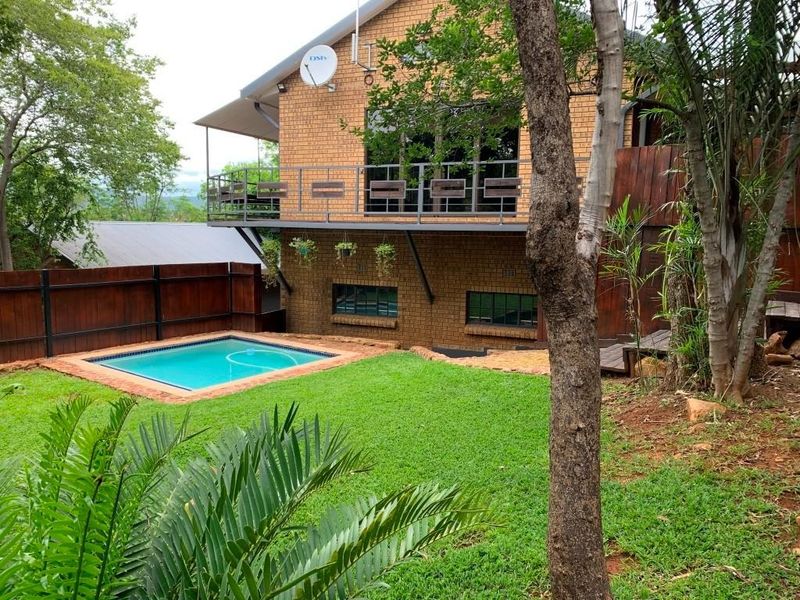 Rear view of the property featuring a brick facade, elevated balcony, swimming pool, and landscaped garden area.
