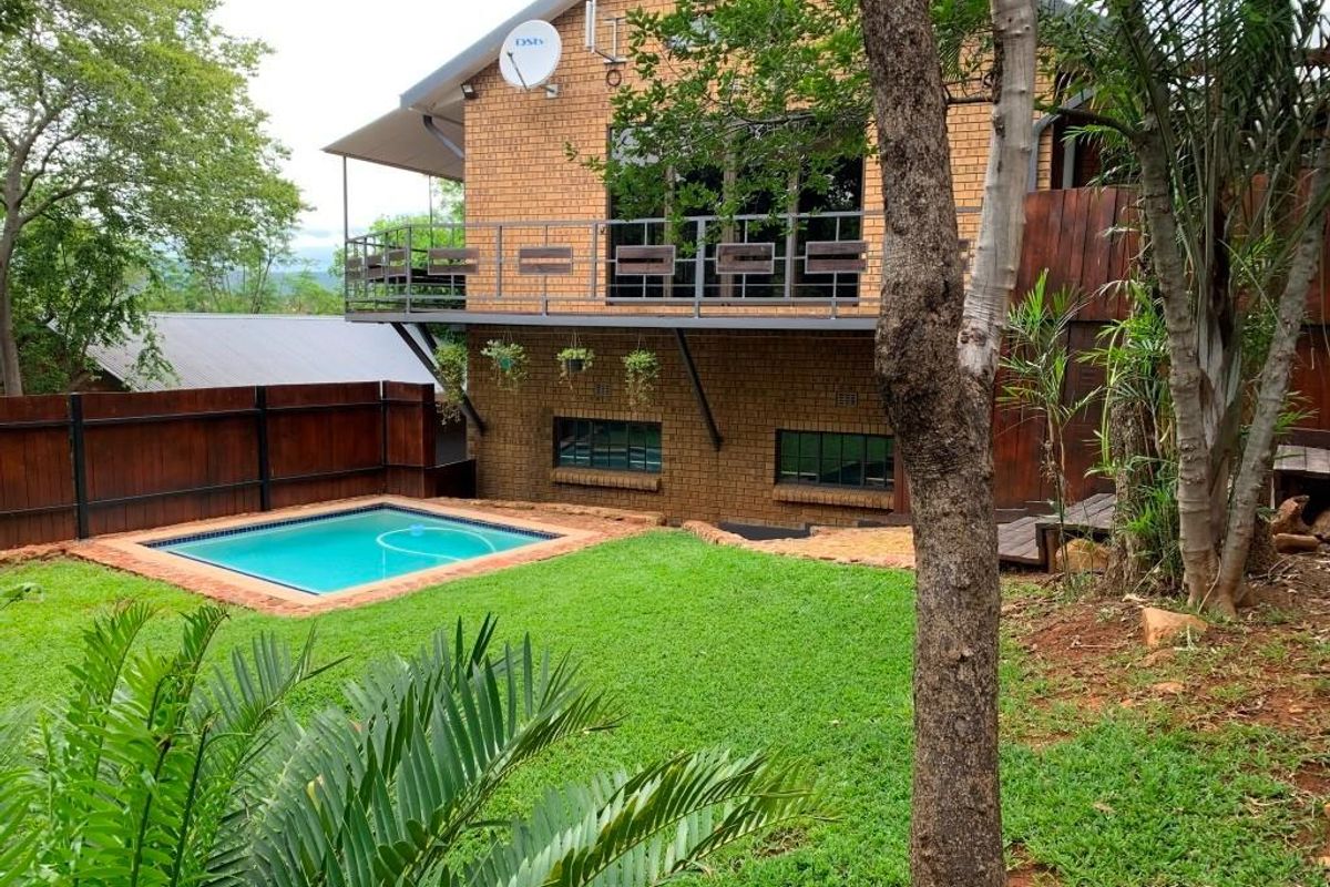 Rear view of the property featuring a brick facade, elevated balcony, swimming pool, and landscaped garden area.